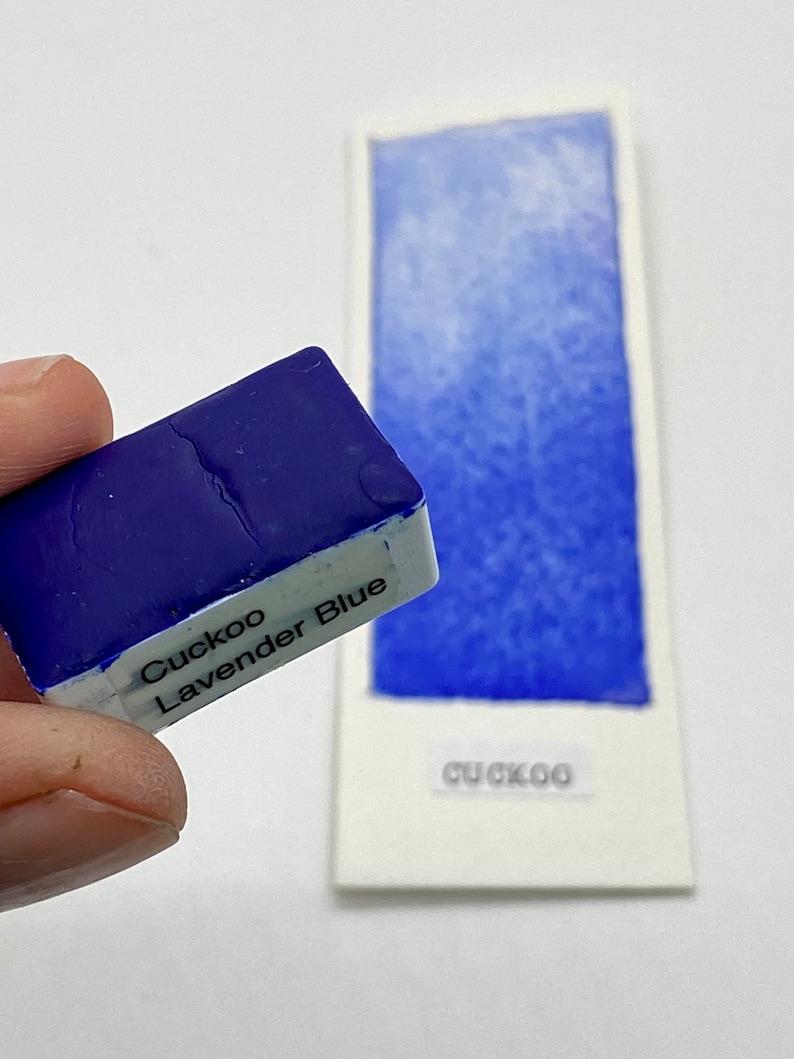 May include: A small, blue watercolor paint pan labeled "Cuckoo Lavender Blue".
