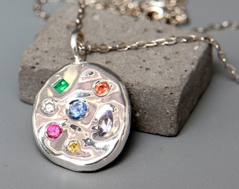 May include: A silver necklace with a round pendant featuring a variety of colorful gemstones, including green, blue, red, and yellow.