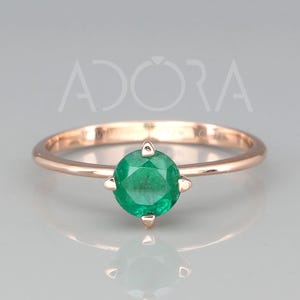 Puede incluir: Un delicado anillo de oro rosa con una piedra preciosa redonda de color verde esmeralda engastada en garras.