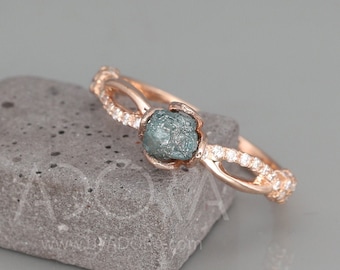 May include: A rose gold ring with a rough, gray diamond set in the center. The band is accented with small, clear diamonds.