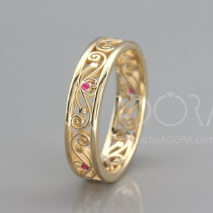 Puede incluir: Una banda de boda de filigrana dorada con pequeñas piedras preciosas rojas engastadas en el diseño.