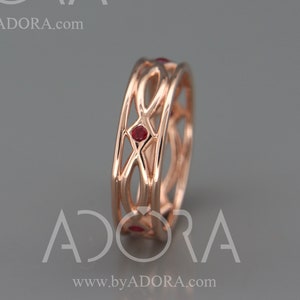 May include: A rose gold ring with a delicate, intricate design featuring a series of connected loops and four small red gemstones.