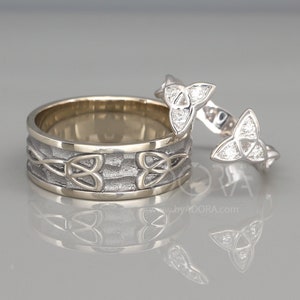 Könnte beinhalten: Ein Paar Eheringe mit einem keltischen Knotendesign. Der Ring links ist ein breiter Ring mit einer strukturierten Oberfläche und einer goldenen Einfassung. Der Ring rechts ist ein dünnerer Ring mit einem keltischen Knotendesign und kleinen Diamanten.