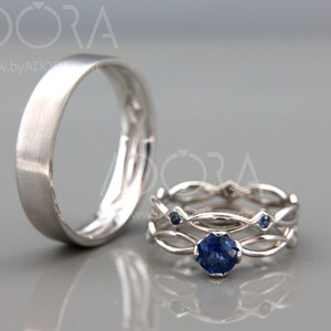 Op de afbeelding: Twee zilveren ringen. E&eacute;n is een eenvoudige band met een geborstelde afwerking. De andere is een set van twee ringen met een verweven ontwerp, met een grote, ronde, donkerblauwe edelsteen en kleinere blauwe accentstenen.
