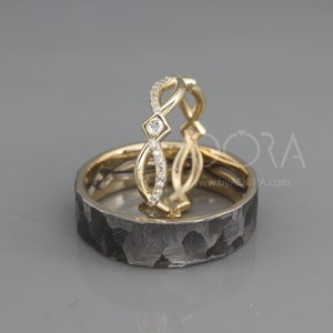 Pode incluir: Duas alian&ccedil;as de casamento, uma com acabamento martelado e a outra com um design delicado encrustado com diamantes. As alian&ccedil;as s&atilde;o de ouro e metal preto.