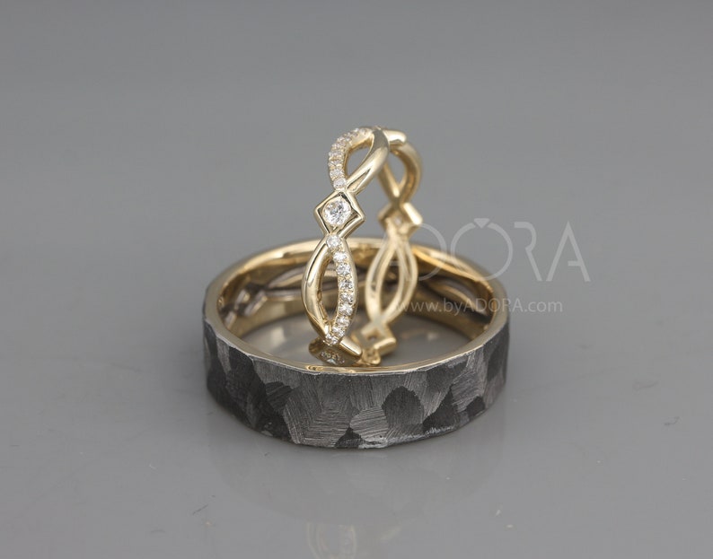Pode incluir: Duas alian&ccedil;as de casamento, uma com acabamento martelado e a outra com um design delicado encrustado com diamantes. As alian&ccedil;as s&atilde;o de ouro e metal preto.