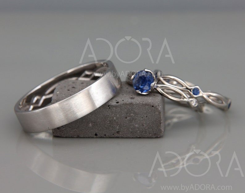 Op de afbeelding: Drie zilveren ringen worden getoond. E&eacute;n ring heeft een geometrisch ontwerp, terwijl de andere twee blauwe edelstenen hebben. E&eacute;n ring heeft een grote, ronde blauwe edelsteen, de andere kleinere blauwe edelstenen. Ze liggen op een grijze ondergrond.