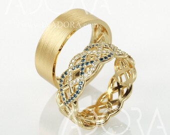 Könnte beinhalten: Zwei goldene Eheringe. Ein Ring ist ein schlichtes, gebürstetes Golddesign. Der andere Ring ist ein filigraneres Design mit einem geflochtenen Muster und blauen und weißen Edelsteinen.