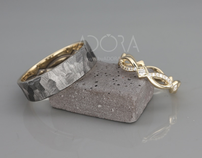 Pode incluir: Duas alian&ccedil;as de casamento, uma com acabamento martelado e a outra com um design delicado de diamantes. As alian&ccedil;as s&atilde;o de ouro e s&atilde;o exibidas em uma pedra cinza.