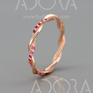 May include: A rose gold band ring with a twisted design and small red gemstones set along the edge.