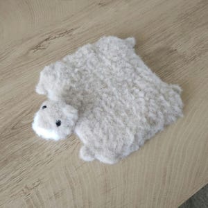 May include: A plush, light gray hippo-shaped pillow with a white snout and black eyes. The pillow is made of a soft, textured material and is lying on a wooden surface.