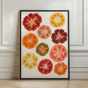 Op de afbeelding: Een ingelijste kunstprint met een verzameling van elf gesneden vleestomaten in diverse kleuren, waaronder dieprood, feloranje, lichtgeel, zachtroze en gevlekt groen, gerangschikt tegen een effen gebroken witte achtergrond.