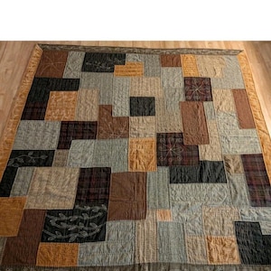 May include: A patchwork quilt with a variety of earth-toned fabrics. The quilt features squares and rectangles in shades of brown, tan, gray, and black. Some squares have embroidered designs. The border has a floral pattern.