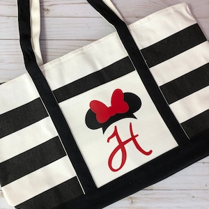 K&ouml;nnte beinhalten: Schwarze und wei&szlig;e gestreifte Tragetasche mit einer roten Schleife und dem Buchstaben "H" in Rot. Die Tasche hat schwarze Henkel.
