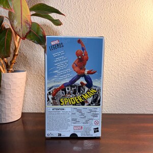 May include: A Marvel Legends action figure box featuring Spider-Man in a dynamic pose. The box is predominantly blue with a cityscape backdrop and the Spider-Man logo. The figure is red and blue.