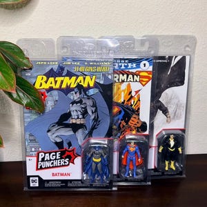 May include: Comic books and action figures featuring Batman, Superman, and Black Adam. The Batman comic book cover has the text "Batman" and "Page Punchers". The action figures are in clear plastic packaging.