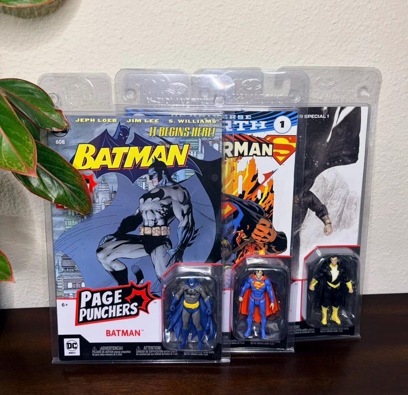 May include: Comic books and action figures featuring Batman, Superman, and Black Adam. The Batman comic book cover has the text "Batman" and "Page Punchers". The action figures are in clear plastic packaging.