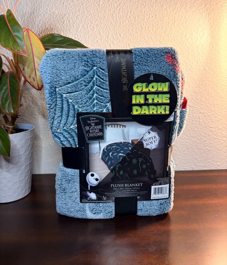 May include: A blue plush blanket featuring a web design and the text "The Nightmare Before Christmas." The blanket is packaged with a black band and a tag that reads "Glow in the Dark!" and "Super Soft!" The blanket measures 60 x 90 inches.
