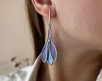 May include: A pair of silver dangle earrings with a blue iridescent glass flower design.