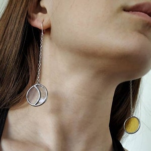 Può includere: Un paio di orecchini pendenti in argento con un design a mezzaluna. Un orecchino ha una luna in vetro trasparente, l'altro ha una luna in vetro giallo.