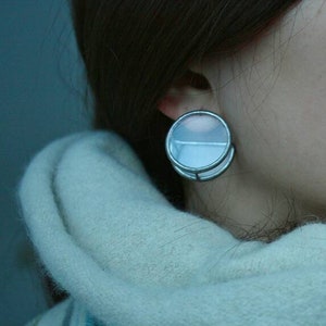 May include: A woman with long brown hair wearing a white and blue striped scarf. She has a large, clear, round, silver-colored ear gauge in her left ear.