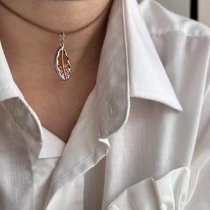 May include: A brown leather choker necklace with a silver pendant shaped like a leaf. The leaf is filled with a translucent orange material.