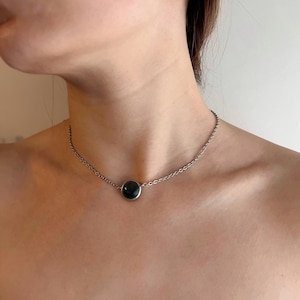 May include: A silver chain necklace with a dark green, circular pendant. The pendant is set in a silver bezel. The necklace is worn around the neck.