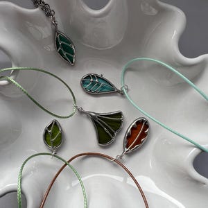 May include: Five leaf-shaped pendants on cords, each with a different colour and design. The pendants are made of stained glass and feature a variety of colours, including green, blue, and orange.