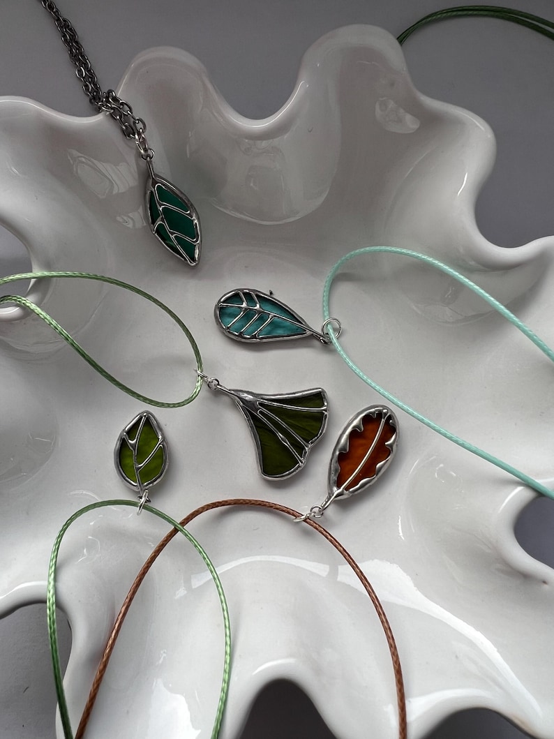 May include: Five leaf-shaped pendants on cords, each with a different colour and design. The pendants are made of stained glass and feature a variety of colours, including green, blue, and orange.