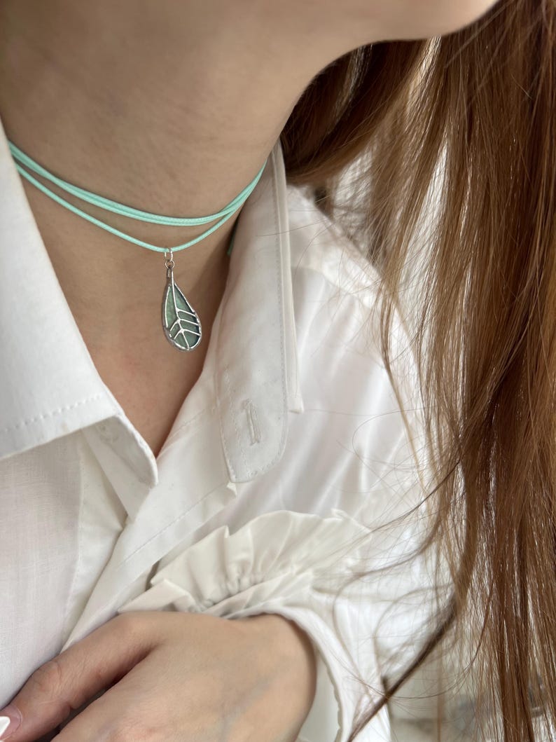 May include: A delicate silver necklace with a light green leaf pendant. The necklace is layered on a light blue cord.