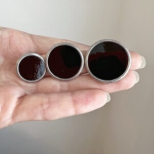 Three sizes of black round enamel disc earrings in hand