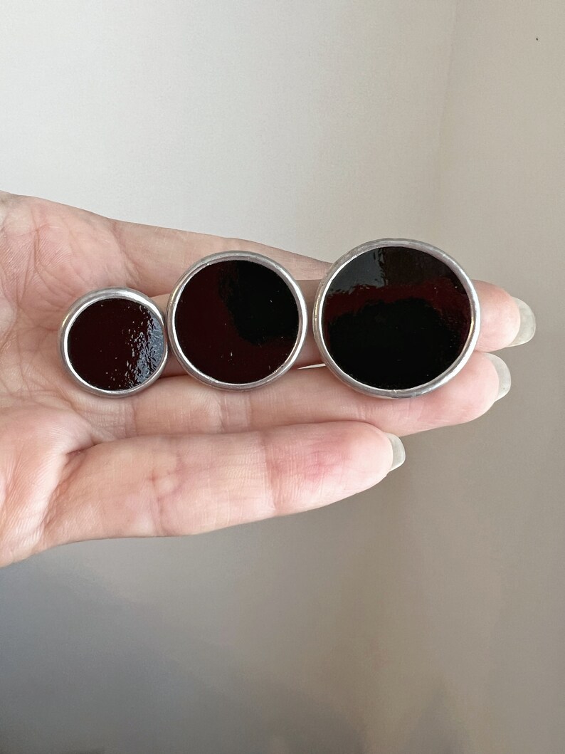 Three sizes of black round enamel disc earrings in hand