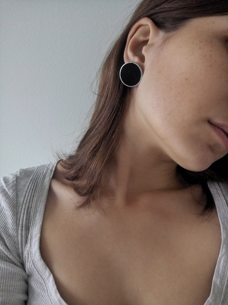 Woman wearing large black round stud earrings minimalist enamel disc close up