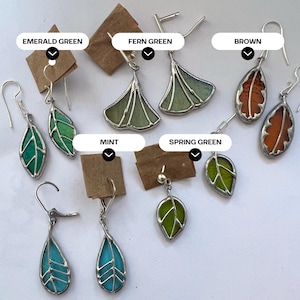 May include: Assortment of stained glass earrings featuring leaf and ginkgo designs in various colours, including emerald green, fern green, brown, mint, spring green, and turquoise.