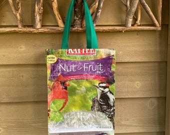 May include: A green tote bag made from recycled birdseed packaging. The bag features a colorful image of a cardinal and a woodpecker with the text "Mille Wild Bird Food Nut & Fruit Blend" printed on the front.