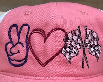 May include: A pink baseball cap with a white mesh back. The front features an embroidered peace sign, heart, and checkered racing flags. The cap has a curved brim and a structured crown.