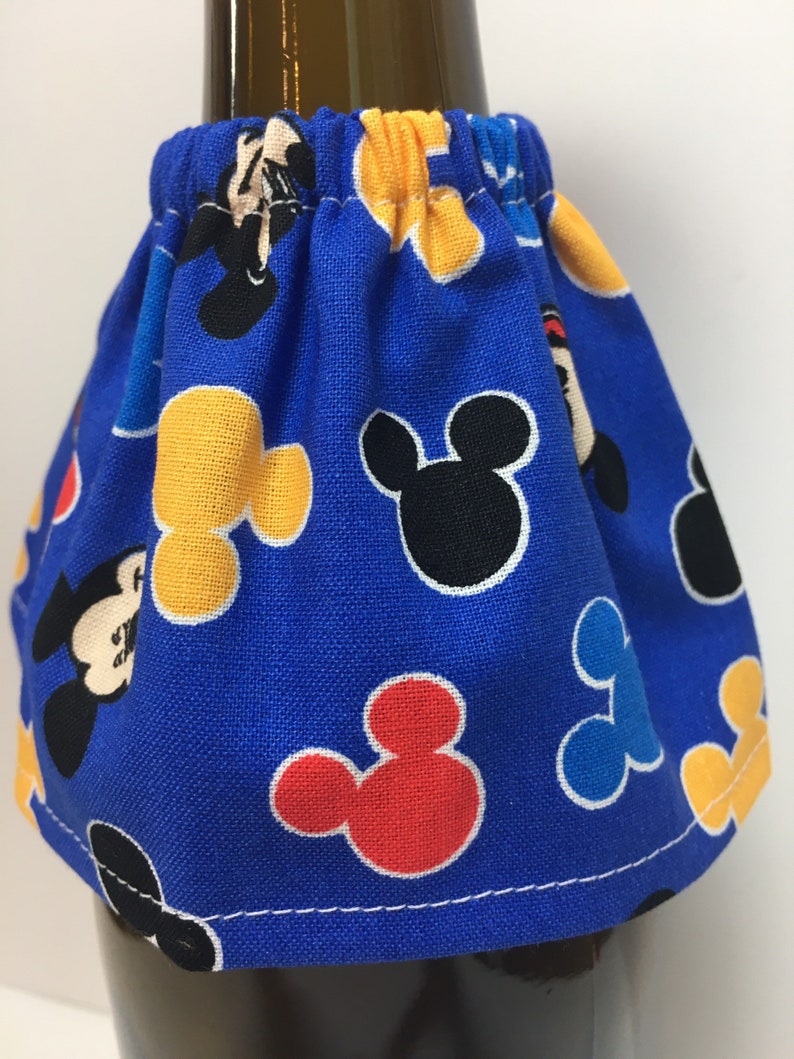 May include: A blue fabric bottle skirt with a repeating pattern of Mickey Mouse heads in black, yellow, red, and blue. The skirt is gathered at the top and has a white stitched hem.