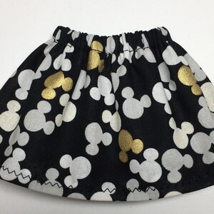 May include: A black skirt featuring a pattern of white and gold Mickey Mouse shapes. It has an elasticated waistband and a zig-zag hem. The fabric is lightweight.