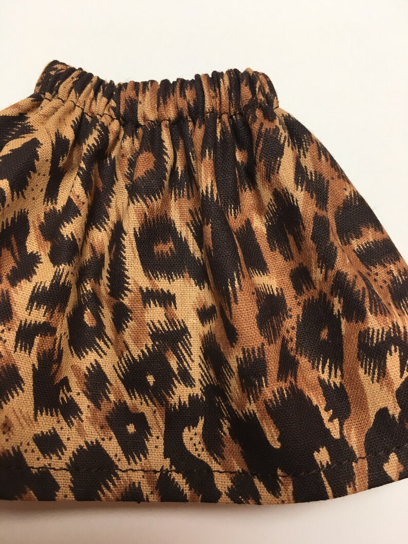 May include: A close-up of a skirt with an elastic waistband. The skirt features a brown and black leopard print pattern. The fabric is gathered at the waistband, creating a ruffled effect. The skirt is made of a lightweight material.