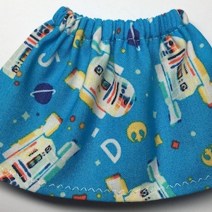 May include: A blue skirt with an elastic waistband, featuring a repeating pattern of white, yellow, and red robot-like figures, planets, and space-themed symbols. The skirt has a white stitched hem.