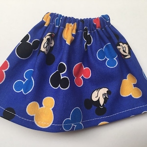 May include: A blue skirt with an elastic waistband, featuring a pattern of Mickey Mouse heads in black, yellow, red, and blue. The skirt is made of a lightweight fabric and has a simple, gathered design.