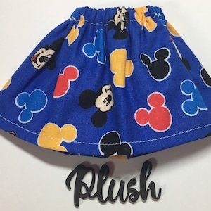 May include: A blue skirt with an elastic waistband, patterned with Mickey Mouse and Mickey Mouse-shaped designs in red, yellow, and black. The word "Plush" is written in a cursive font below the skirt.