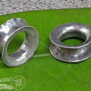 Op de afbeelding: Twee zilveren ringen met een brede, platte band en een afgerond, open midden. De ringen zijn glad en hebben een licht getextureerd oppervlak.