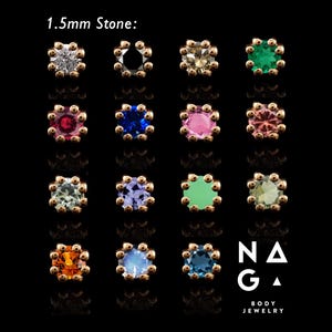 Könnte beinhalten: Eine Auswahl an 1,5 mm Steinstiften für Körperschmuck in verschiedenen Farben, darunter transparent, schwarz, grün, blau, rosa und orange. Jeder Stift hat eine goldfarbene Fassung mit dekorativem Rand. Das Naga Body Jewelry Logo ist sichtbar.