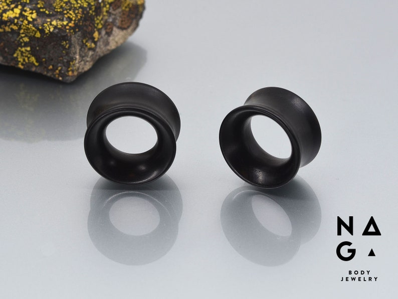May include: Two black wooden ear gauges, also known as plugs or tunnels, are shown on a white surface. The gauges are round and have a slightly flared edge.