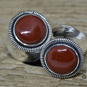 May include: A pair of silver earrings with a red stone set in each. The earrings have a decorative border around the stone.