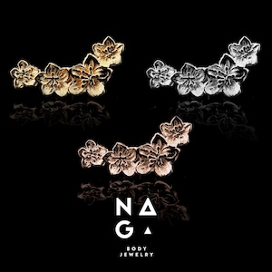 May include: Three floral body jewelry pieces in gold, silver, and rose gold are displayed against a black background. Each piece features a cluster of five flower-shaped designs. The brand name "NAGA BODY JEWELRY" is at the bottom.
