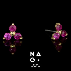 Könnte beinhalten: Ein Paar goldene Körperschmuck-Stecker mit jeweils drei rosafarbenen Edelsteinen, die in einer dreieckigen Form angeordnet sind.