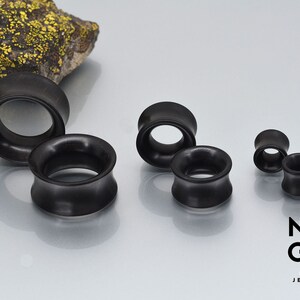 May include: A set of five black wooden ear gauges of varying sizes. The gauges are smooth and have a slightly flared design.