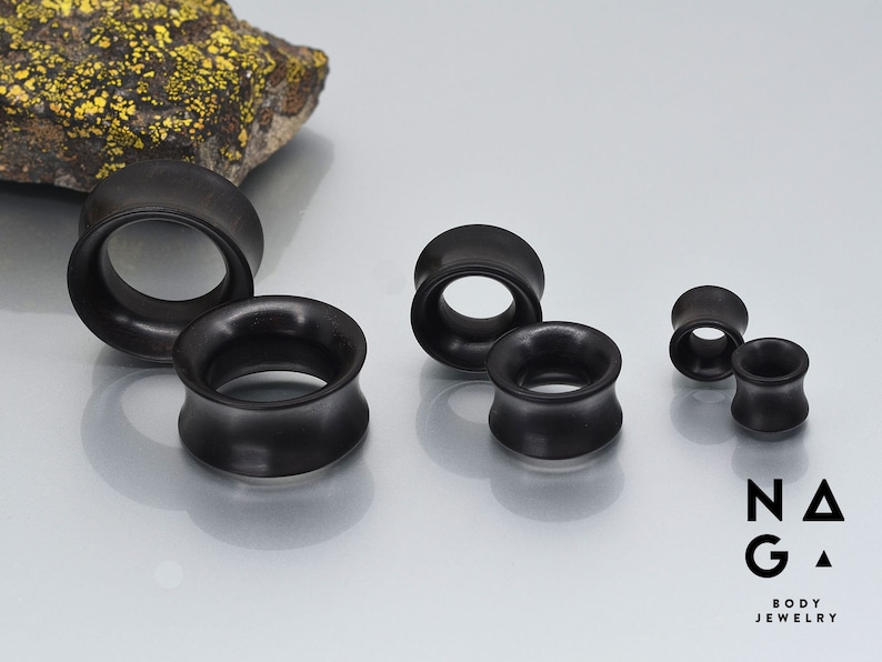 May include: A set of five black wooden ear gauges of varying sizes. The gauges are smooth and have a slightly flared design.